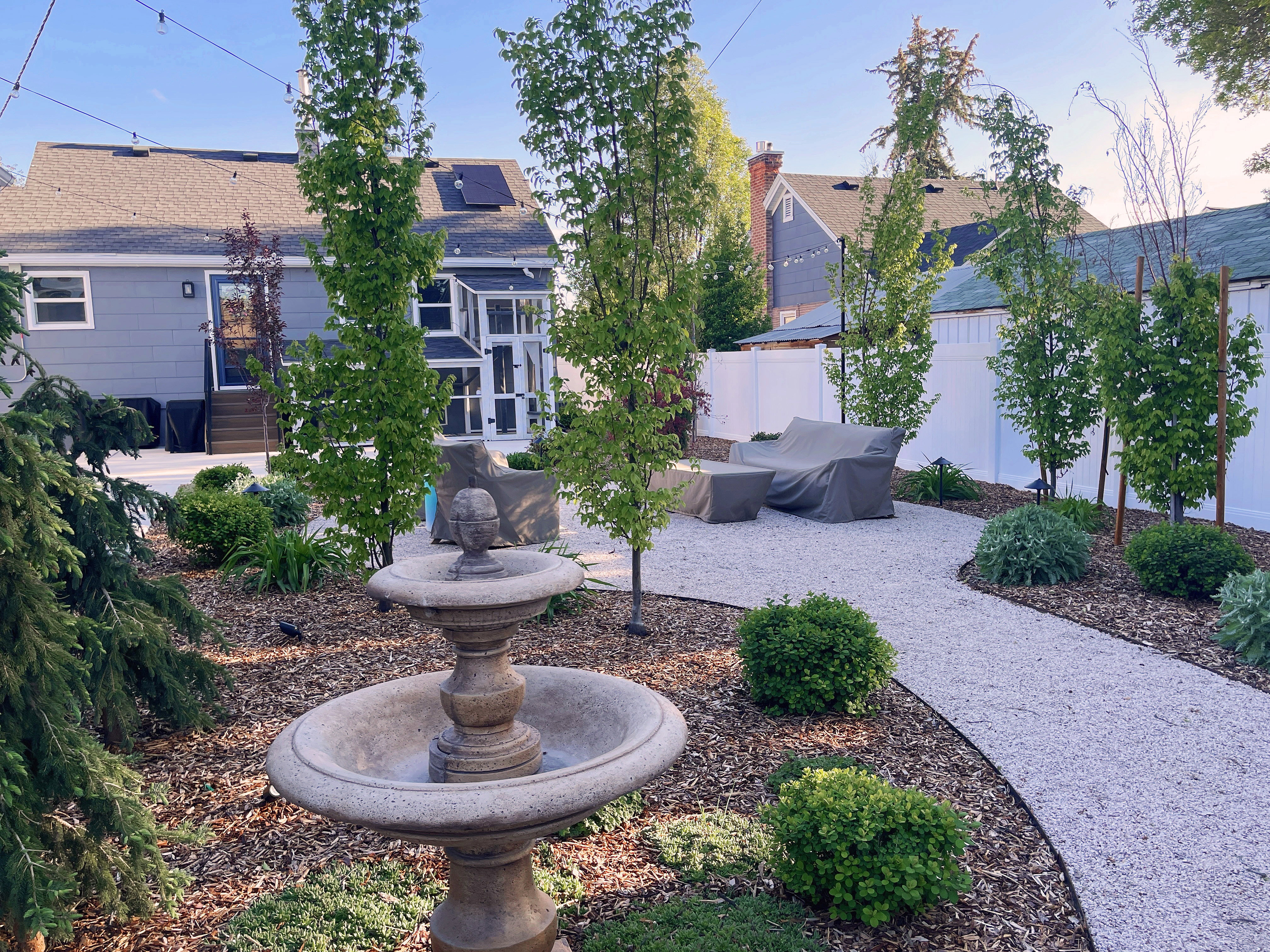 Landscaped backyard featuring a stone fountain, gravel pathways, and mature greenery