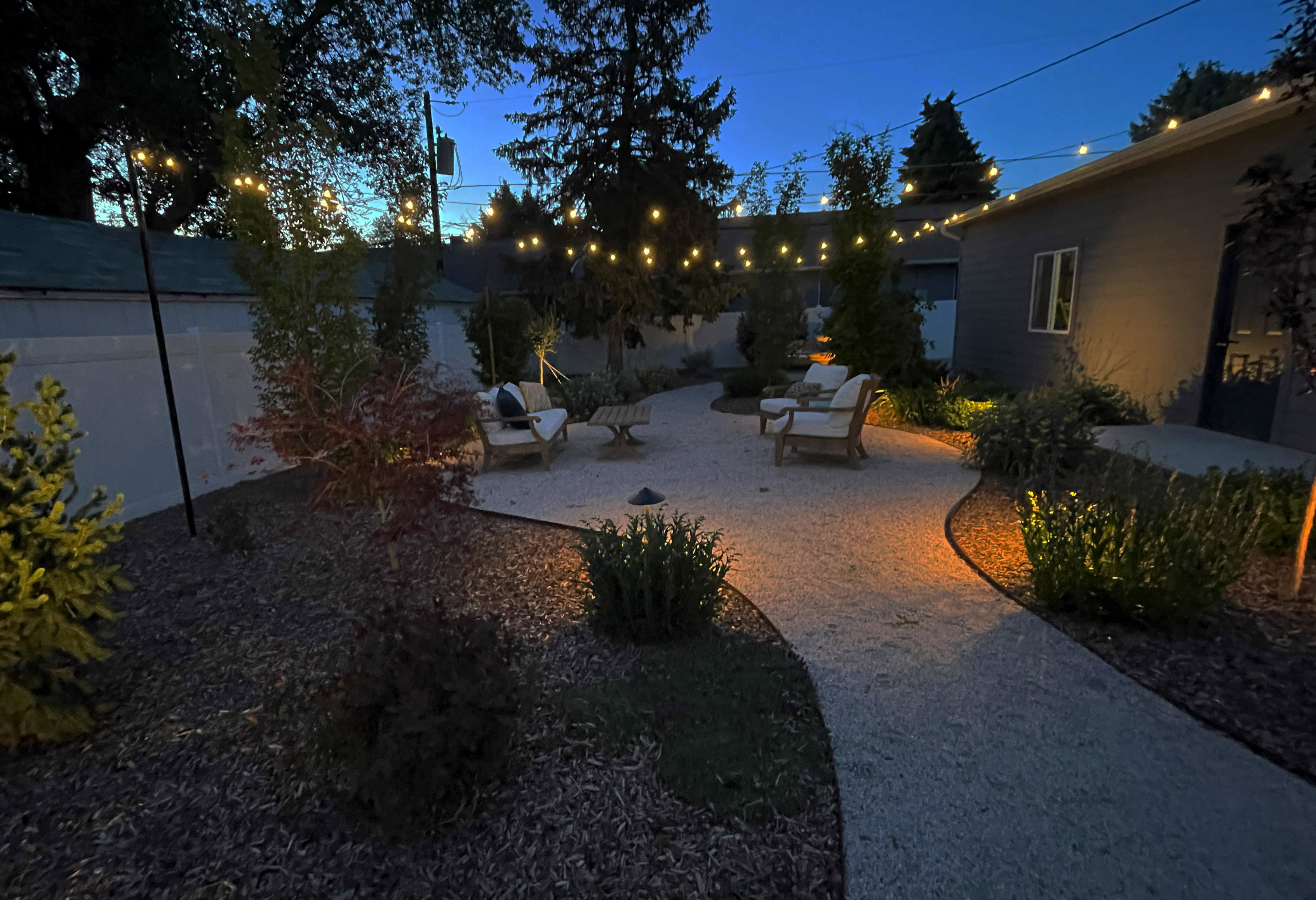 Outdoor patio area featuring string lighting, a gravel pathway, and integrated landscape lighting