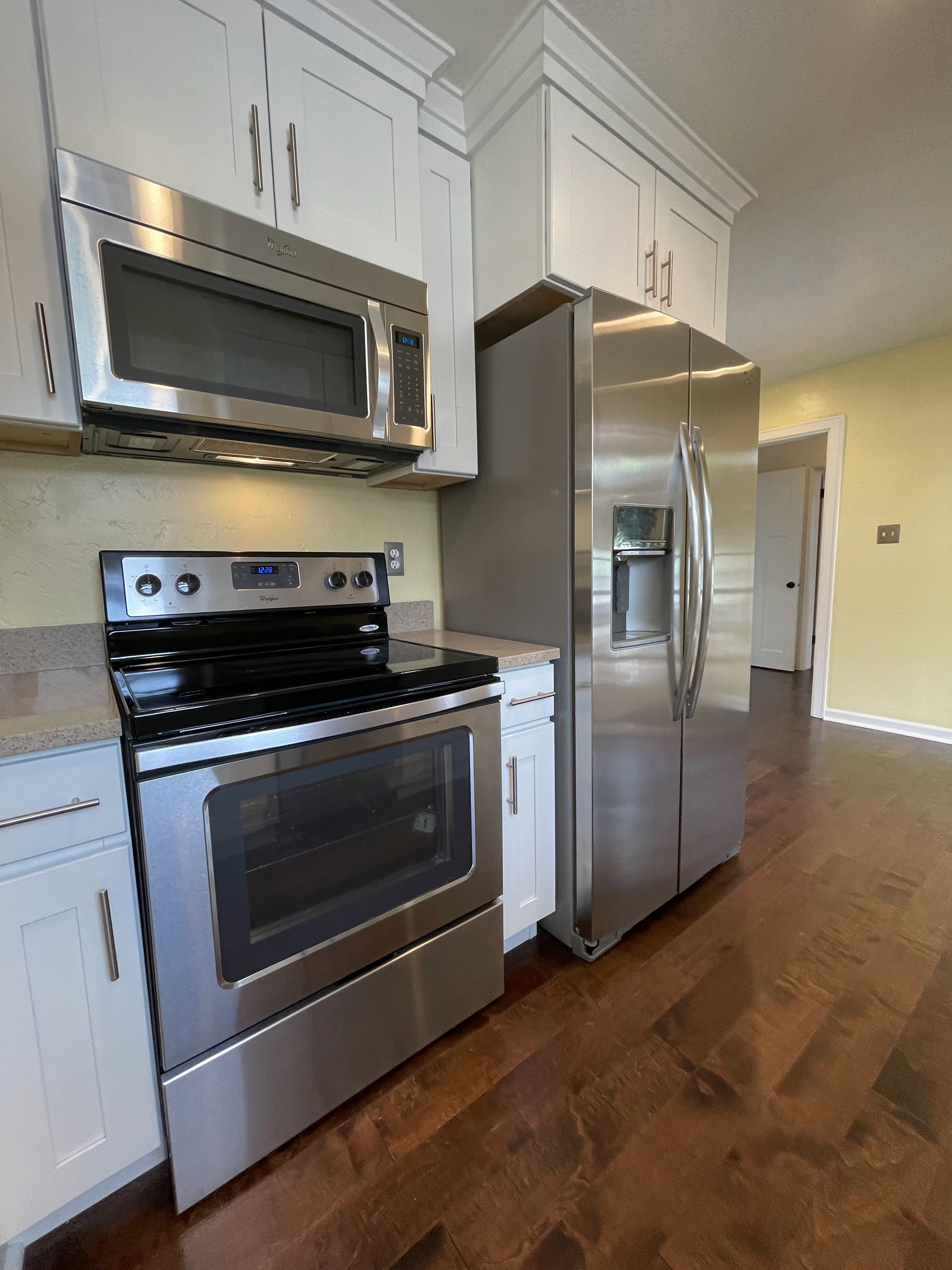 Kitchen featuring white shaker-style cabinetry with crown molding, stainless steel appliances, light-toned countertops, and wood-finish flooring