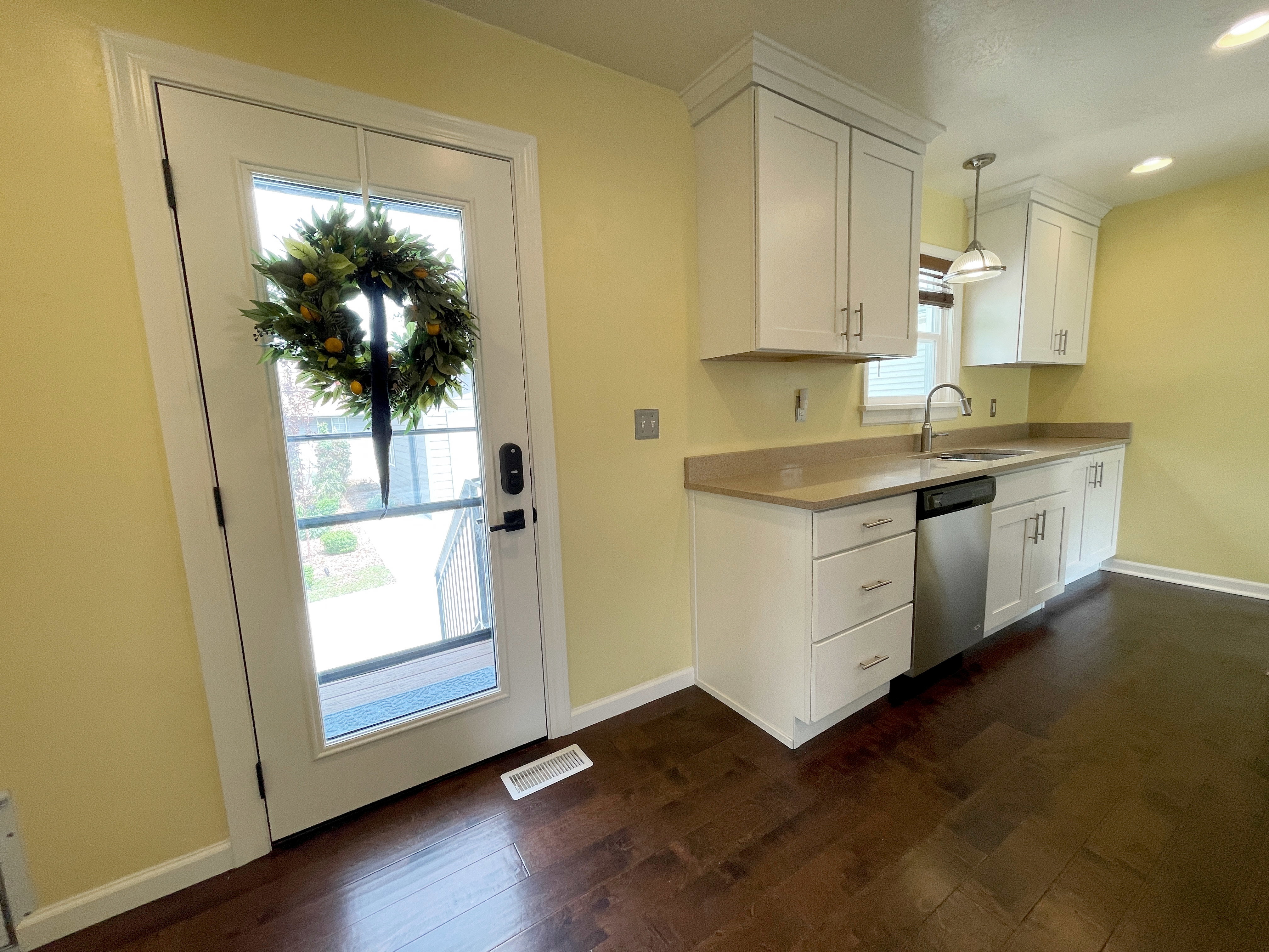 Kitchen featuring wood-finish flooring, white cabinetry with crown molding, light-toned countertops, and a stainless steel sink with a pull-down faucet