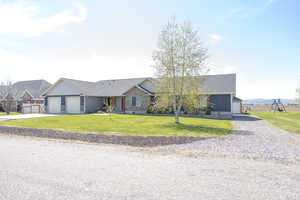 Ranch-style home featuring gravel driveway, a front lawn, roof with shingles, and stone siding