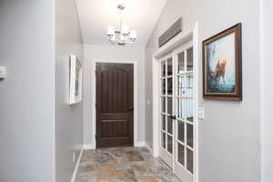 Foyer with stone finish flooring, suspended lighting, and vaulted ceiling