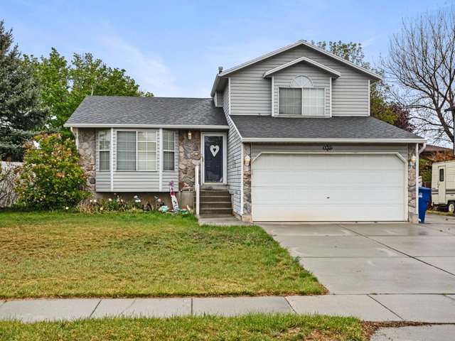 Tri-level home with a front lawn, a garage, concrete driveway, a shingled roof, and stone siding