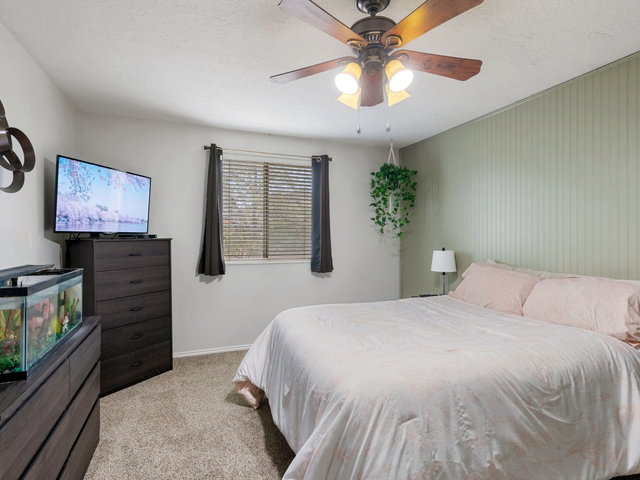 Bedroom with light carpet, ceiling fan, and a textured ceiling