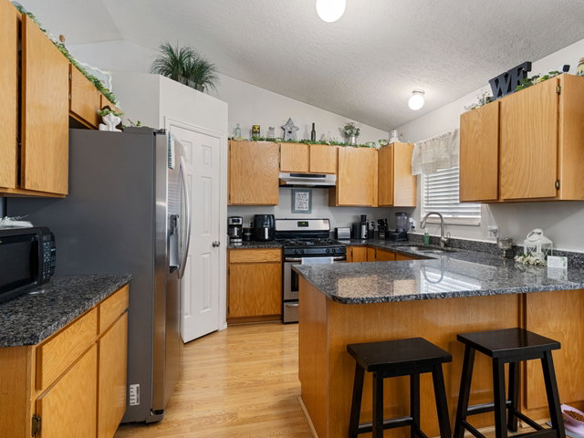 Kitchen featuring a peninsula, wood finish cabinets, stainless steel appliances, light wood-style floors, and dark stone countertops