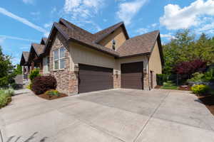 View of property exterior with stone siding, concrete driveway, a garage, and stucco siding