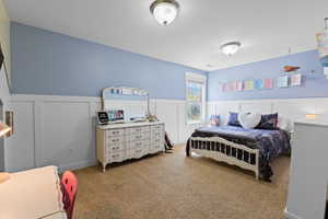 Bedroom featuring a decorative wall, a wainscoted wall, and light colored carpet