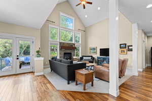 Living room featuring light wood finished floors, french doors, ceiling fan, a fireplace, and vaulted ceiling