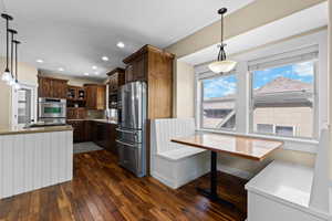 Kitchen featuring breakfast area, stainless steel appliances, pendant lighting, light stone countertops, and dark wood-style flooring