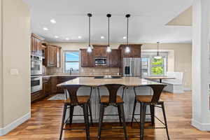Kitchen with a kitchen bar, stainless steel appliances, a kitchen island, hanging light fixtures, and light stone counters