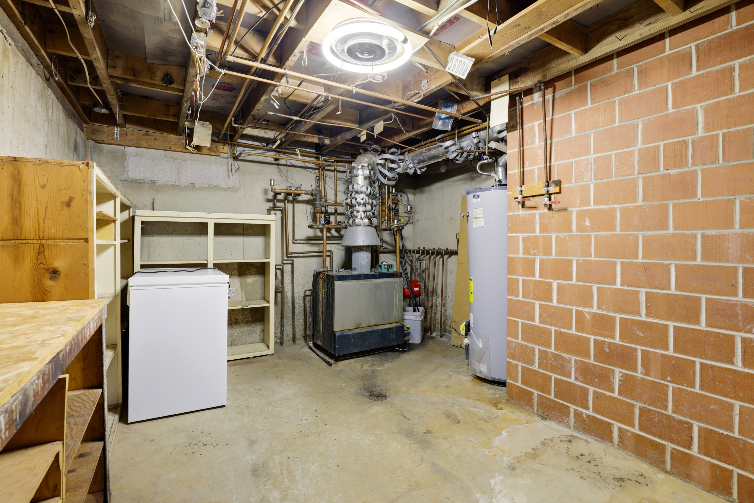 Unfinished below grade area with white refrigerator and water heater