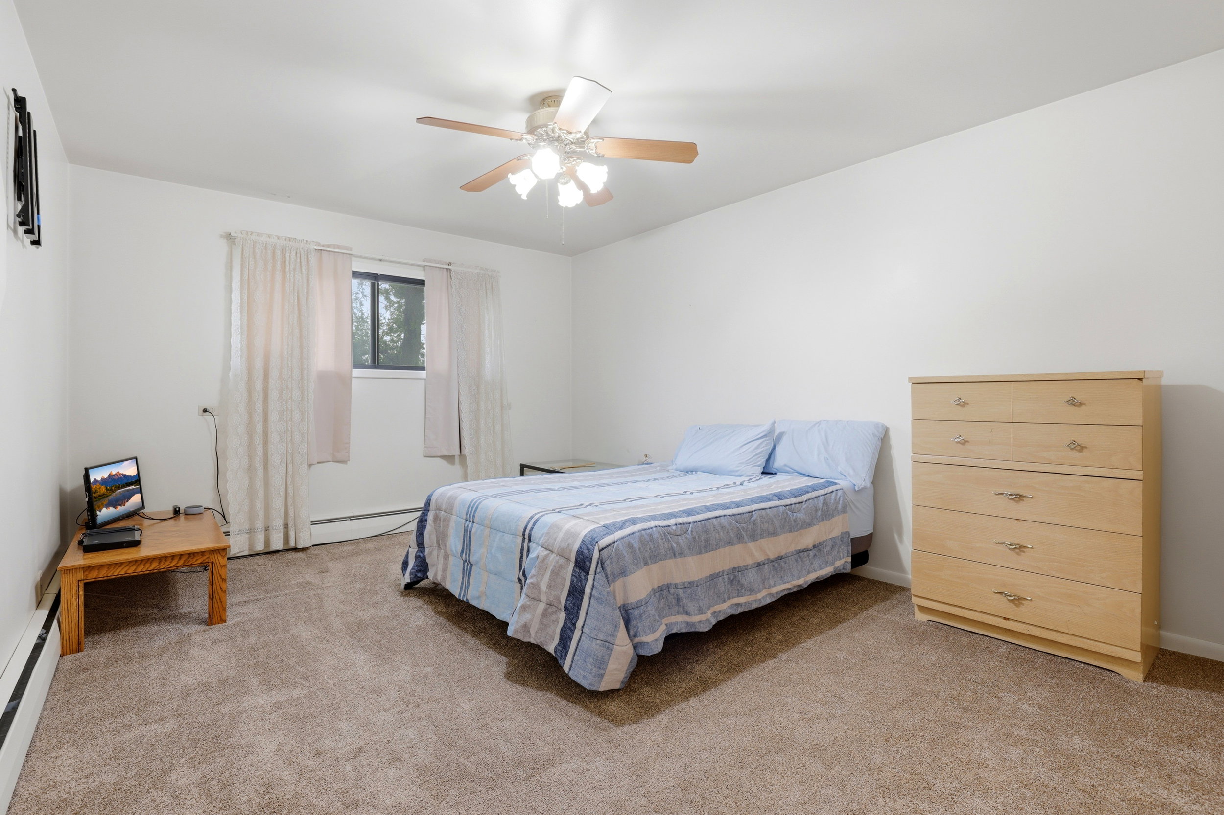 Bedroom with light carpet, ceiling fan, and a baseboard heating unit