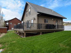 Rear view of property featuring a yard, a wooden deck, and a shingled roof
