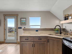 Kitchen featuring light stone countertops, healthy amount of natural light, light wood finished floors, and lofted ceiling
