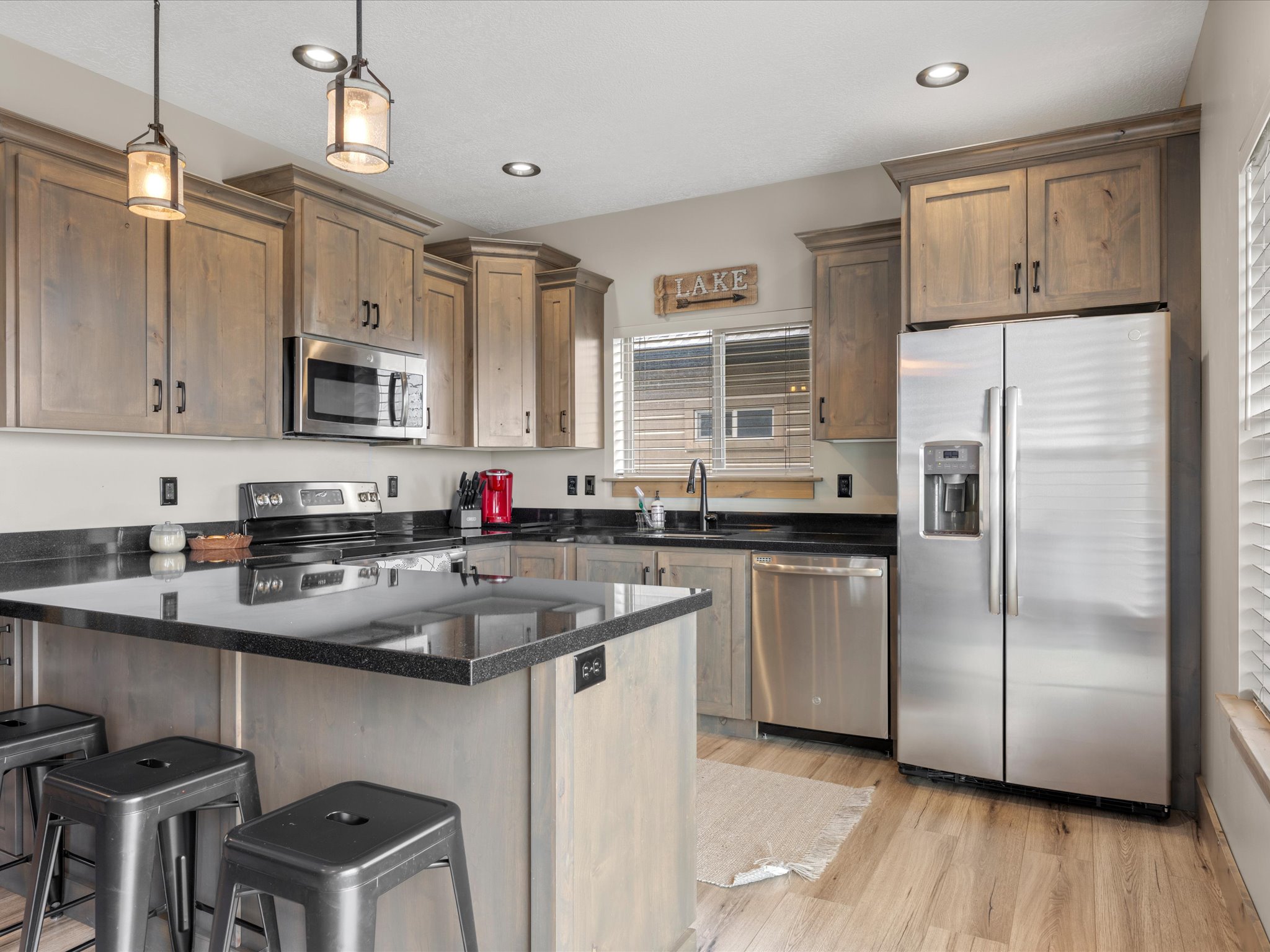 Kitchen featuring stainless steel appliances, a breakfast bar, dark stone counters, light wood-style flooring, and decorative light fixtures