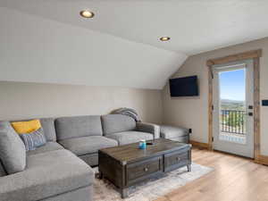 Living room with light wood-style flooring, lofted ceiling, and recessed lighting