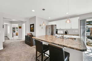 Kitchen area with a breakfast bar area, freestanding refrigerator, light carpet, white cabinets, and decorative light fixtures