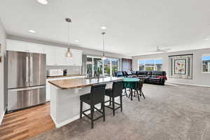 2nd partial kitchen featuring freestanding refrigerator, white cabinetry, a kitchen island with sink, a breakfast bar area, and open floor plan with views out on the deck