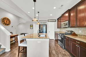 Kitchen area of the great room featuring a breakfast bar area, a center island with sink, light stone counter tops, stainless steel appliances, and a textured ceiling