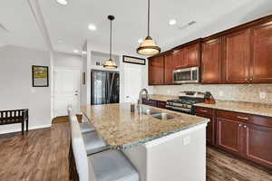 Kitchen featuring stainless steel appliances, light stone countertops, dark wood-type flooring, and a center island with sink