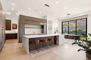 Kitchen featuring pendant lighting, modern cabinets, a spacious island, light stone countertops, and a kitchen bar