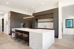 Kitchen featuring modern cabinets, light stone countertops, stainless steel appliances, a kitchen breakfast bar, and a spacious island