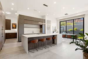 Kitchen featuring hanging light fixtures, modern cabinets, a large island, light stone counters, and a kitchen bar