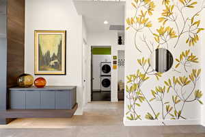 Hall with stacked washing machine and dryer, concrete floors, and recessed lighting