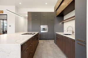 Kitchen featuring modern cabinets, light stone countertops, stainless steel appliances, decorative backsplash, and recessed lighting