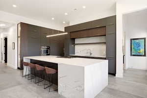 Kitchen with modern cabinets, light stone countertops, stainless steel appliances, a breakfast bar, and recessed lighting