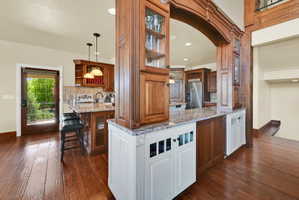 Two tone kitchen featuring light stone counters, glass insert cabinets, high end fridge, open shelves, and two tone cabinets