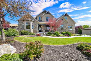 View of front of property with stone siding, a front yard, covered porch, and stucco siding