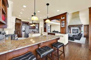 Two tone kitchen featuring light stone countertops, a breakfast bar area, a fireplace, glass insert cabinets, and stainless steel appliances