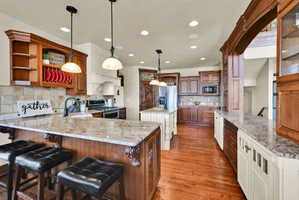 Dual tone kitchen with a peninsula, a kitchen breakfast bar, two tone cabinets, stainless steel appliances, and light stone countertops