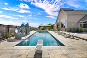 View of pool with a water slide, a fenced backyard, a diving board, and patio surround