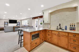 Kitchen featuring a peninsula, backsplash, a breakfast bar area, wood finish cabinets, and light stone countertops