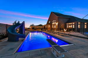 Pool at dusk featuring a water slide, a fenced backyard, an outdoor pool, and a patio