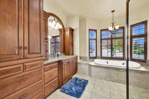 Bathroom with a chandelier, vanity, a garden tub, and light tile patterned flooring