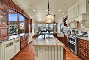 Kitchen with double oven range, light stone counters, tasteful backsplash, dark wood finished floors, and dual tone cabinets