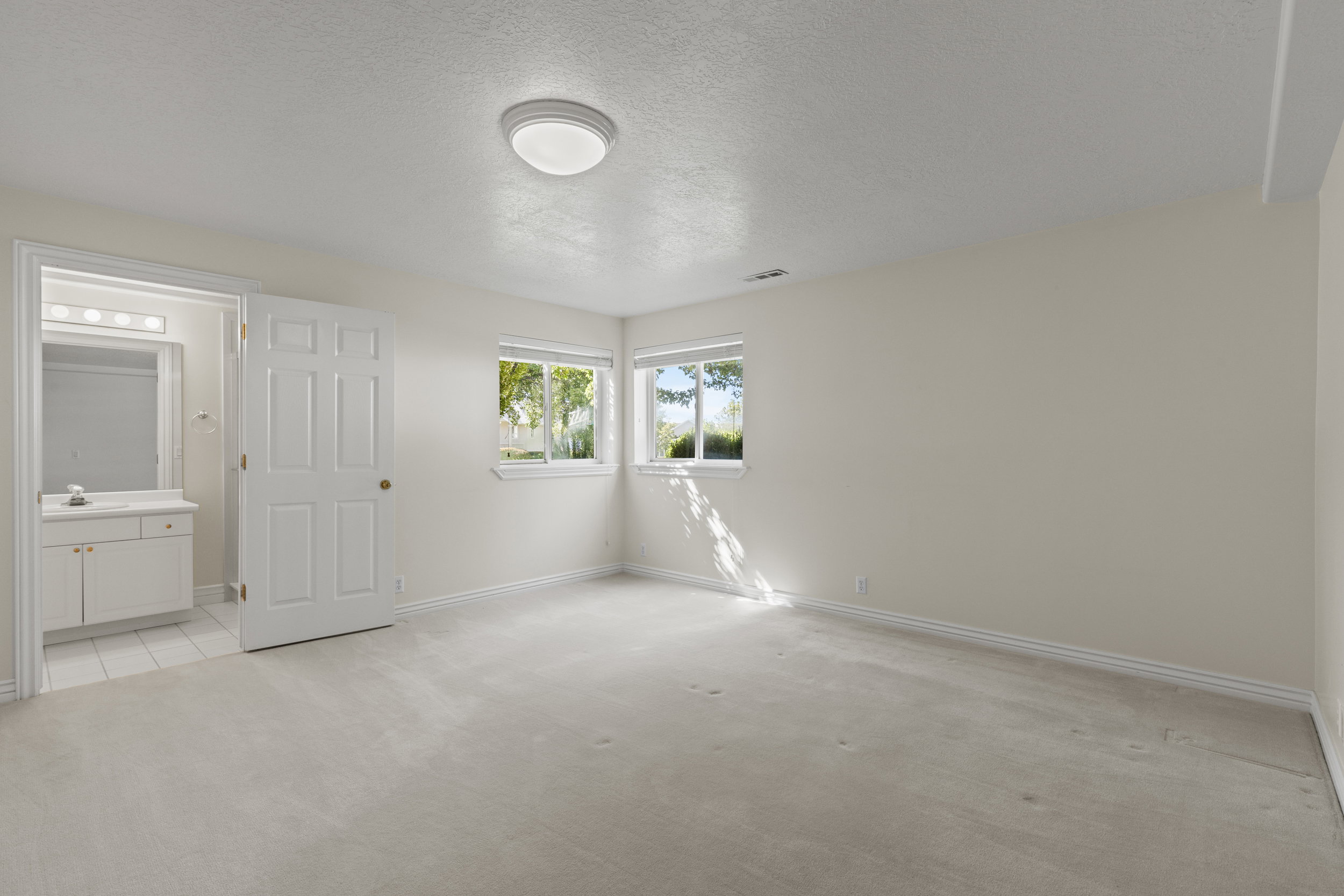 Unfurnished bedroom with a textured ceiling, light carpet, and ensuite bath