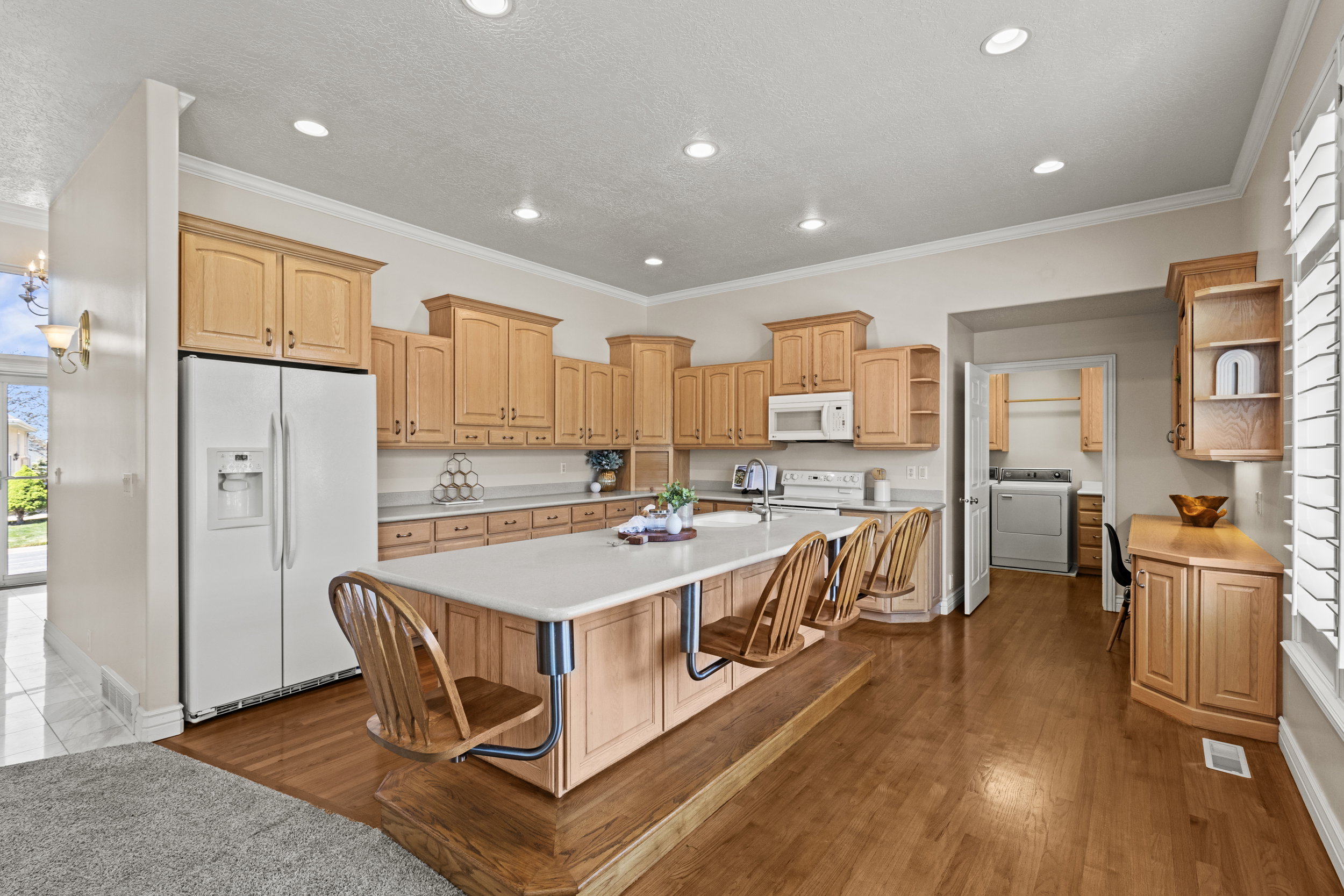 Kitchen with white appliances, light countertops, open shelves, dark wood finished floors, and a kitchen island with sink