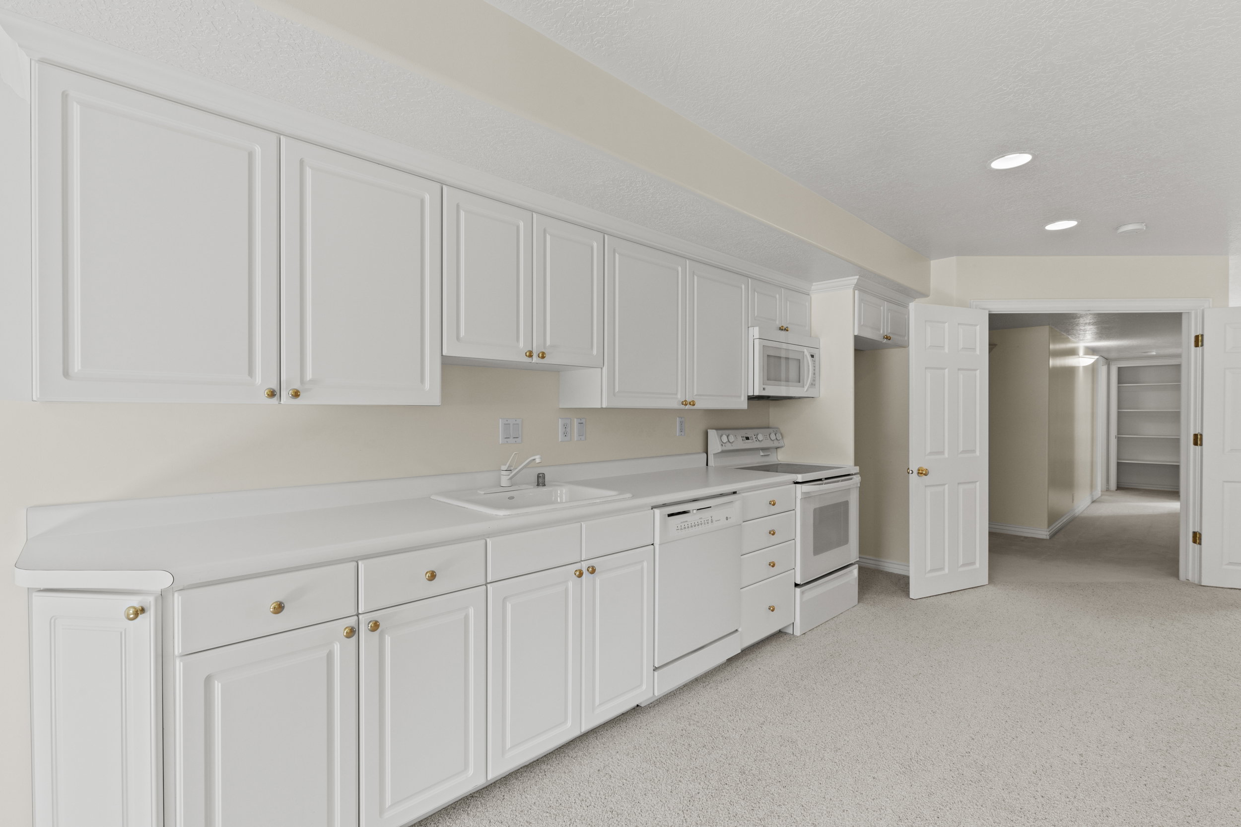 Kitchen with white cabinetry, white appliances, light countertops, light colored carpet, and recessed lighting