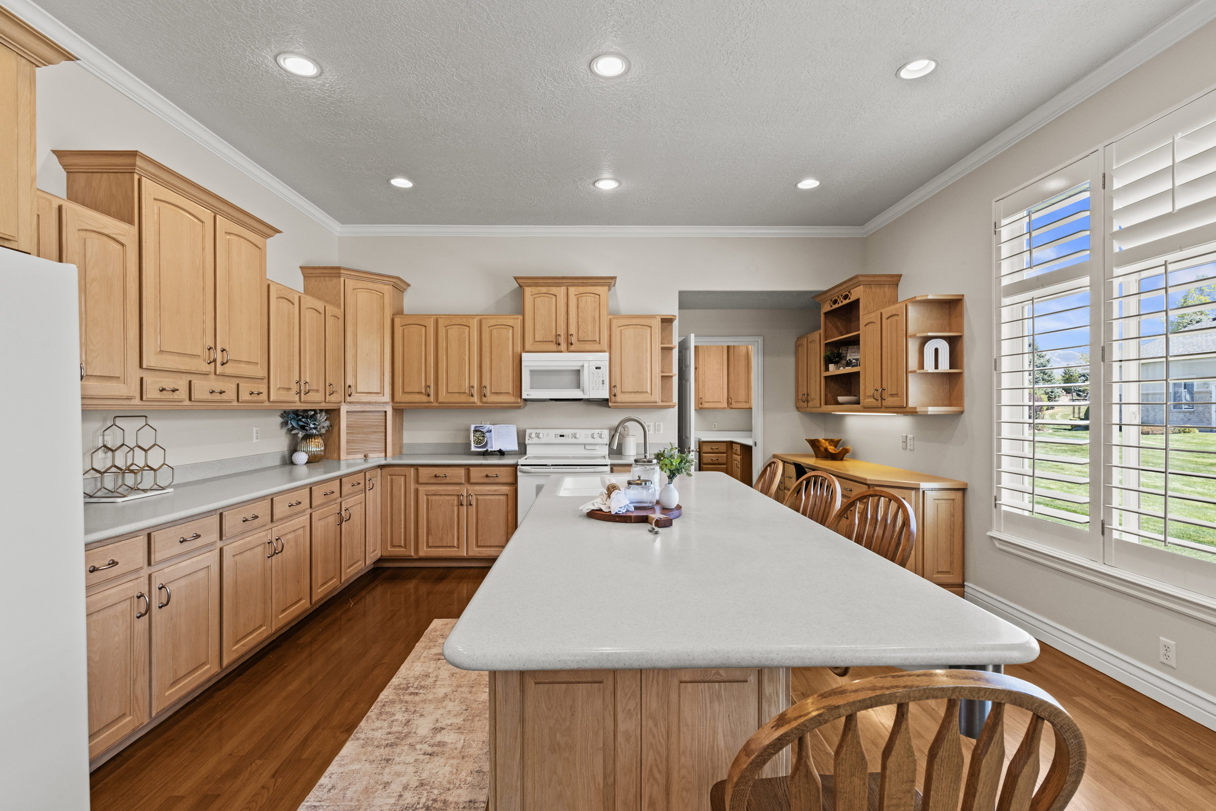 Kitchen with open shelves, white appliances, light countertops, dark wood-style flooring, and crown molding