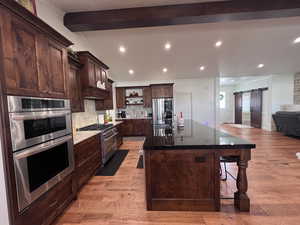 Kitchen with a barn door, dark wood finish cabinetry, stainless steel appliances, vaulted ceiling with beams, and a large island