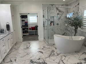 Bathroom with a walk in closet, crown molding, a soaking tub, vanity, and a marble finish shower