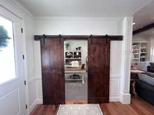 Hall with dark wood-style flooring, a barn door, ornamental molding, and a decorative wall