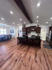 Kitchen featuring a breakfast bar area, a large island with sink, dark wood finish cabinetry, backsplash, and stainless steel appliances
