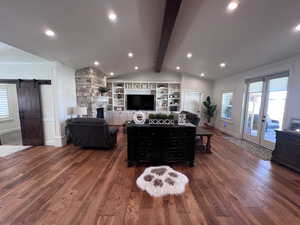 Living area featuring a barn door, french doors, lofted ceiling with beams, a fireplace, and wood finished floors
