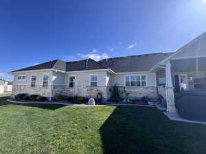 Back of house featuring a yard, stone siding, and roof with shingles