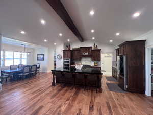 Kitchen with dark wood finish cabinetry, a spacious island, stainless steel appliances, a kitchen breakfast bar, and light wood-style flooring